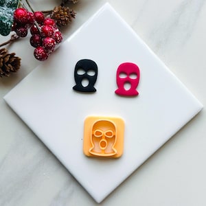 May include: Three silicone moulds for making fondant or polymer clay masks. The moulds are shaped like a ski mask with a hole for the eyes and mouth. One mould is black, one is red, and one is orange.