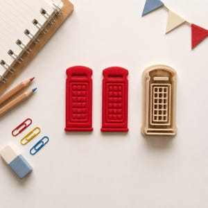 May include: Two red plastic telephone booth cookie cutters and one beige plastic telephone booth cookie cutter mould. The items are shaped like classic British telephone boxes with a rectangular structure and a grid pattern on the front panel.