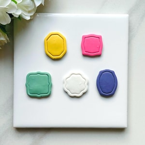 May include: Six different colored clay shapes, each with a decorative border. The shapes are a yellow octagon, a pink rectangle, a green rectangle, a white scalloped shape, a purple oval, and a blue oval.