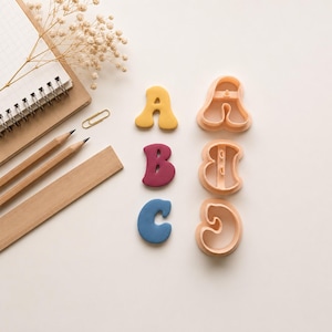 Può includere: Tre forme di lettere solide in giallo, bordeaux e blu, insieme a tre stampini per biscotti in plastica abbinati per le lettere A, B e C. Il set è disposto con un taccuino a spirale, due matite in legno e una graffetta dorata.