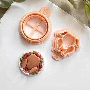 以下が含まれることがあります： 3つのピーチ色のクッキーカッター：十字のデザインの丸いもの、七面鳥の形をしたカッター、フロスティングと緑で飾られた七面鳥のクッキー。カッターはベーキング用で、白い表面にあります。