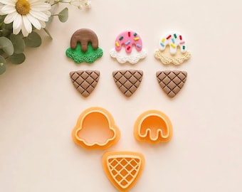 May include: Three ice cream cone shapes made of clay with textured details, including one with green and brown, one with pink and white with sprinkles, and one with white and tan with sprinkles, alongside three orange plastic cookie cutters.