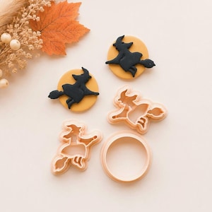 May include: Two black witch silhouettes on yellow circular discs, two light peach witch-shaped cookie cutters, and one light peach circular cookie cutter. The items are arranged together, showcasing the shapes and the finished decorative pieces.