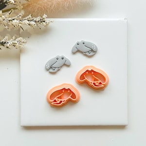 May include: Four pieces: two grey sea creature-shaped decorations and two orange crab-shaped cookie cutters. The decorations have small white dots and black eyes. The cutters have a layered design. The items are on a white surface.