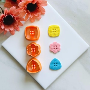 Peut inclure: Un assortiment d'emporte-pièces en plastique orange de formes carrées, fleuries et triangulaires, ainsi que des boutons colorés et texturés. Les boutons sont jaunes, roses et bleus. Des fleurs décoratives orange sont en arrière-plan.