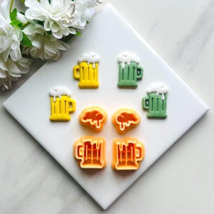 May include: Set of six cookie cutters shaped like beer mugs. The cutters are in three colours: green, yellow, and orange.