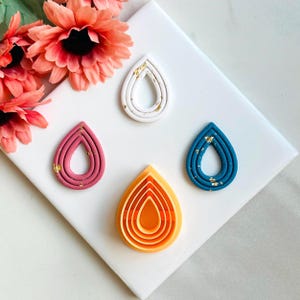 May include: Four teardrop-shaped polymer clay earring blanks with gold flecks. The blanks are layered in shades of white, pink, blue, and orange.