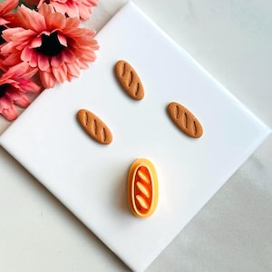 May include: Four brown miniature bread cookie cutters and one orange miniature bread cookie cutter on a white surface.