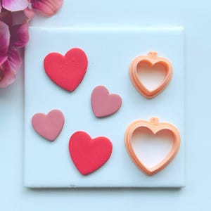 May include: A set of three ceramic mugs with a speckled, cream-colored glaze. Each mug features a different hand-painted design: a blue and green leaf, a yellow flower, and a red berry. The mugs have a simple, rounded shape.