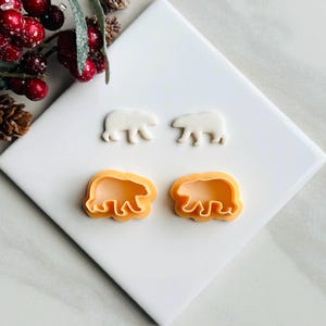 May include: Two white plastic bear cookie cutters and two orange plastic bear cookie cutters on a white surface.