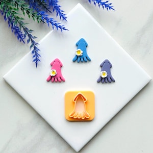 May include: A set of three fondant cutouts shaped like squids with a flower on top. The cutouts are pink, blue, and purple. A plastic cookie cutter shaped like a squid is also included.