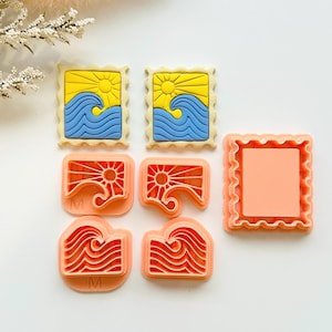 May include: A collection of cookie cutters in various shapes. Two are rectangular with a yellow sun, blue waves, and a yellow border. Four are peach-colored, depicting a sun and waves. One peach-colored cutter is a blank rectangle with a scalloped edge.
