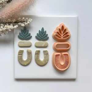 May include: A collection of polymer clay earring components and cutters. The clay pieces are in shades of green, beige, and yellow, with a textured, ribbed design. The cutters are in a peach color and feature leaf and geometric shapes.