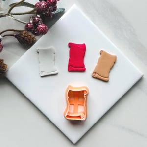 Puede incluir: Tres cortadores de galletas con forma de rollo enrollado. Uno es blanco, otro rojo y otro beige. Los cortadores están sobre una superficie blanca.