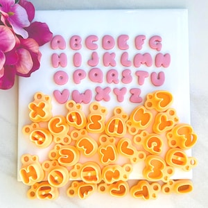 Könnte beinhalten: Ein Satz Alphabet-Ausstecher in Rosa und Gelb. Die Ausstecher haben die Form von Großbuchstaben. Die rosa Ausstecher sind alphabetisch geordnet, während die gelben Ausstecher verstreut sind.