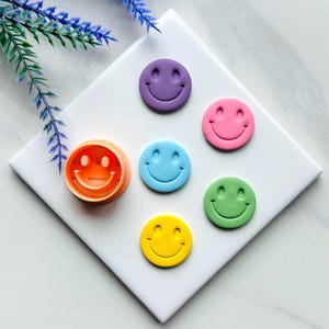 以下が含まれることがあります： 紫、ピンク、青、緑、黄色のスマイリーフェイスとオレンジ色のスマイリーフェイスのクッキーカッターを含む、6つのカラフルなスマイリーフェイスのクッキーカッターのセット。