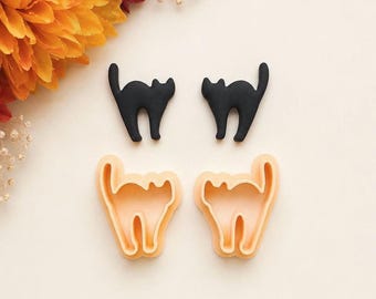 May include: Two solid black cat-shaped cutters and two light orange cat-shaped cookie cutters. The black cutters are opaque and smooth, while the light orange cutters have an open frame design with a raised edge for cutting dough shapes.