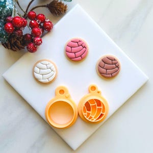 May include: Three small, round, colourful clay ornaments with a detailed design, resembling Mexican pastries. Two yellow plastic cookie cutters, one with a smooth surface and the other with a detailed design, are also shown.