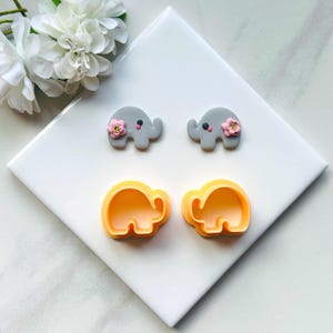 May include: Two gray elephant-shaped cookie cutters with pink flowers and two yellow elephant-shaped cookie cutters.