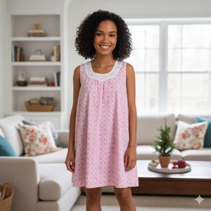 May include: A sleeveless pink nightgown with a white lace trim around the neckline. The nightgown has a geometric pattern and is knee-length. The person in the image is smiling and standing in a well-lit living room.