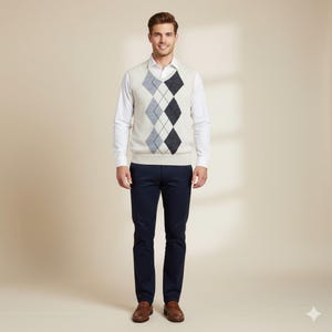 May include: A man in a cream argyle sweater vest with navy, light blue, and black diamond patterns, a white shirt, and navy trousers. The man is smiling. The outfit is a classic style.