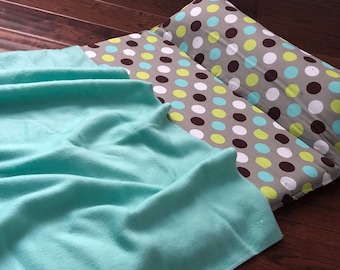 May include: A turquoise fleece blanket is draped over a gray and white polka dot patterned floor cushion with a matching pillow.