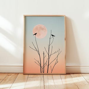 May include: A framed print with a minimalist design featuring two black birds perched on bare branches against a backdrop of a large, pink moon and a gradient sky transitioning from blue to orange.