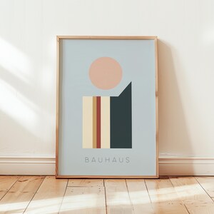 Könnte beinhalten: Gerahmter Bauhaus-Kunstdruck mit geometrischen Formen in gedeckten Farben. Das Design umfasst einen pfirsichfarbenen Kreis, eine dunkelgrüne Form und ein vertikales Rechteck mit Streifen. Das Wort "BAUHAUS" ist unten aufgedruckt.