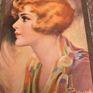 May include: A vintage postcard featuring a woman with short, red hair. She is wearing a colorful scarf and looking to the side. The text "There's a song in my heart" is printed at the bottom of the postcard.
