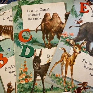 May include: A vintage children's book with colorful illustrations of animals and letters. The book features a giraffe, a camel, a donkey, a deer, and an elephant. The text on the pages reads: "A is for June", "B is for Hunt", "C is for Camel. Roaming the sands.", "D is", "E is for Elephant. Huge and gray", and "F is for Fawn. Romping all day."