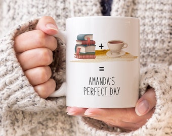 Può includere: Tazza in ceramica bianca con una grafica di una pila di libri e una tazza di caffè. Il testo sulla tazza recita "Amanda's Perfect Day".