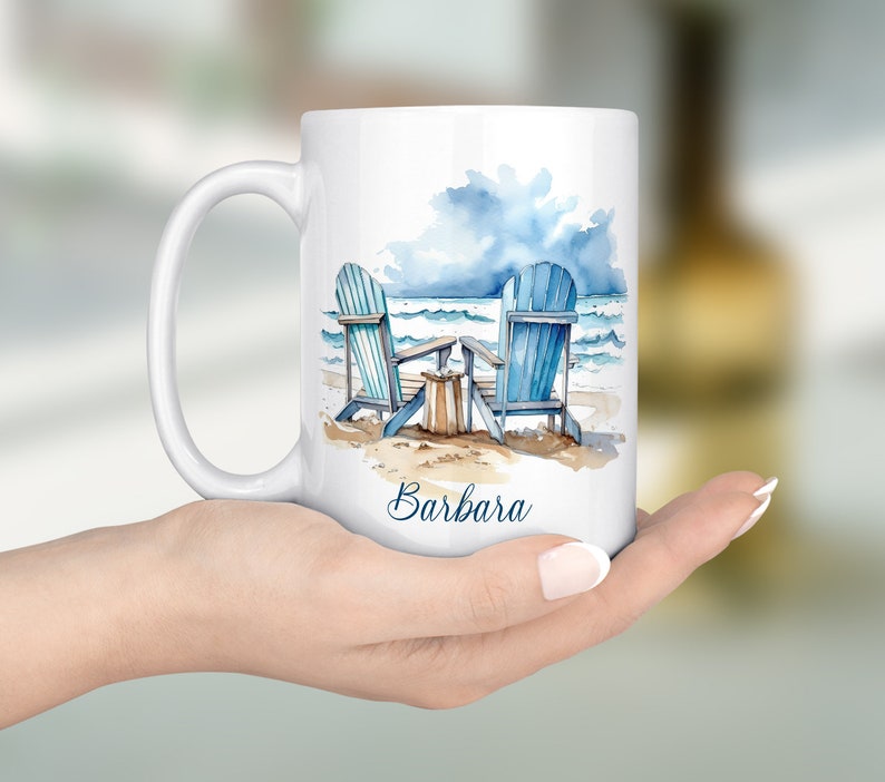 Peut inclure: Une tasse en c&eacute;ramique blanche avec une illustration aquarelle de deux chaises Adirondack bleues sur une plage avec un ciel nuageux et le nom "Barbara" imprim&eacute; au bas.