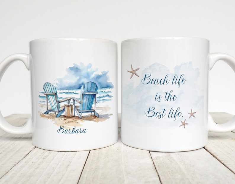Peut inclure: Une tasse en c&eacute;ramique blanche avec une illustration aquarelle de deux chaises de plage bleues sur une plage de sable avec des vagues oc&eacute;aniques en arri&egrave;re-plan. Le texte "Barbara" est imprim&eacute; sur la tasse. L'autre c&ocirc;t&eacute; de la tasse a une illustration aquarelle d'un ciel bleu avec des nuages et le texte "Beach life is the best life." avec deux &eacute;toiles de mer.