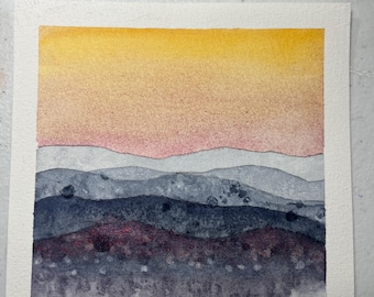 Könnte beinhalten: Aquarellmalerei einer Landschaft mit einem Himmel, der von Gelb nach Rosa übergeht. Darunter sind geschichtete blaue und violette Berge dargestellt, mit einem dunkleren, strukturierten Vordergrund. Das Kunstwerk befindet sich auf strukturiertem, weißem Papier.