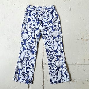 A pair of vintage blue and white, straight leg, mid rise jeans with a large, allover paisley print and a button fly front.
