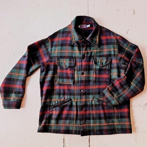 Könnte beinhalten: Ein grünes, rotes und schwarzes kariertes Flanellhemd mit Knopfleiste und zwei großen Taschen.