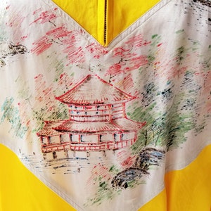 Puede incluir: Una camisa amarilla y blanca con un dise&ntilde;o pintado de una pagoda japonesa y un paisaje. La camisa tiene una cremallera en la parte delantera.