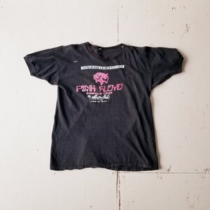 K&ouml;nnte beinhalten: Schwarzes T-Shirt mit einem rosa Schweine-Motiv und dem Text "Pink Floyd Animals Tour" mit dem Datum "June 18 1977".