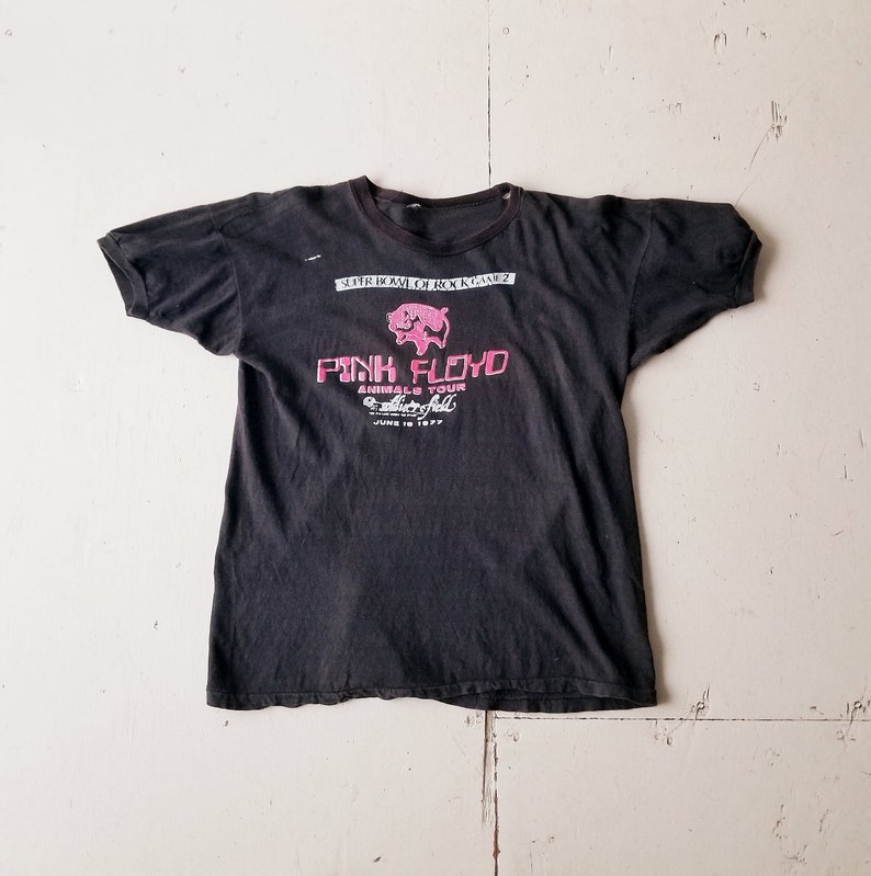 K&ouml;nnte beinhalten: Schwarzes T-Shirt mit einem rosa Schweine-Motiv und dem Text "Pink Floyd Animals Tour" mit dem Datum "June 18 1977".