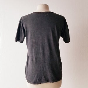 K&ouml;nnte beinhalten: Ein dunkelgraues T-Shirt mit kurzen &Auml;rmeln auf einer Puppe.