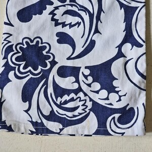 May include: Close-up of white fabric with a navy blue floral pattern. The design features stylized leaves and flower shapes. The fabric has a visible texture and a clean hemline.