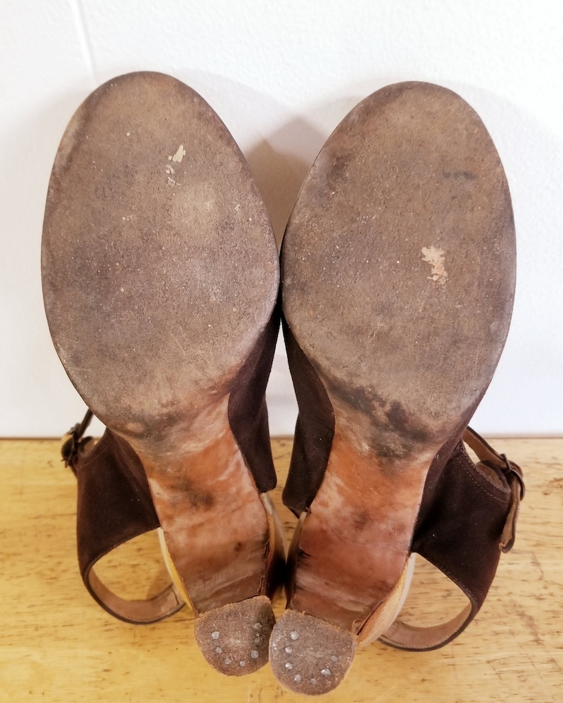 May include: A pair of brown suede heeled sandals with ankle straps. The soles are worn and show signs of use.