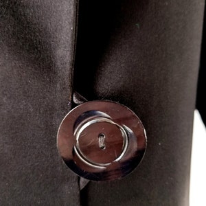 May include: A black satin fabric with a large, round, black button. The button has a raised, circular design and a small hole in the centre.