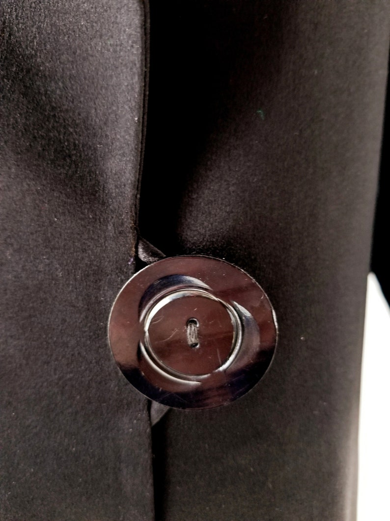 May include: A black satin fabric with a large, round, black button. The button has a raised, circular design and a small hole in the centre.