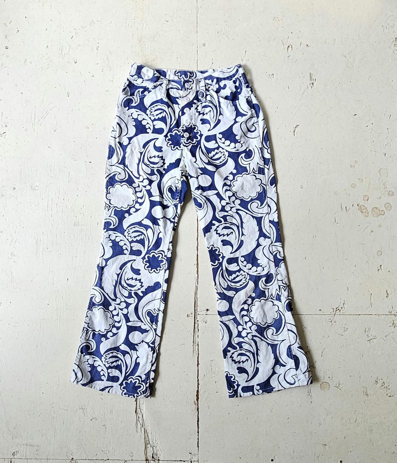A pair of vintage blue and white, straight leg, mid rise jeans with a large, allover paisley print and a button fly front.