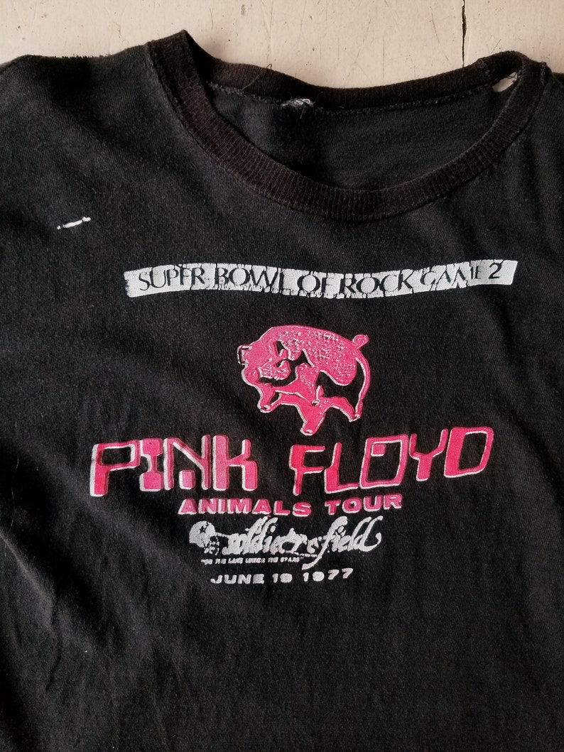 K&ouml;nnte beinhalten: Schwarzes T-Shirt mit einem rosa Schweine-Motiv und dem Text "Pink Floyd Animals Tour Soldier Field June 19 1977".