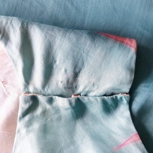 May include: A light blue fabric with a pink and white tie-dye pattern. The fabric has a seam with two silver metal snaps.