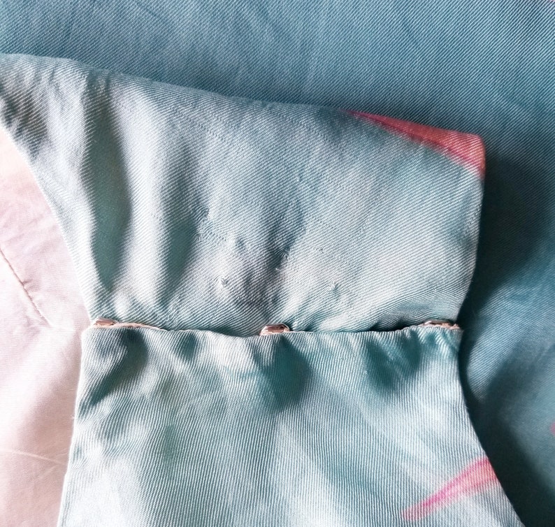 May include: A light blue fabric with a pink and white tie-dye pattern. The fabric has a seam with two silver metal snaps.