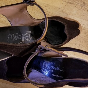May include: A pair of brown suede heeled shoes with ankle straps. The shoes have a black leather insole with the text "Shingert Shoes Rapids, Mich." on one shoe and "Footwear by Sohasl Reg.U.S.Pat.Off." on the other shoe.