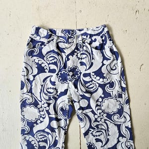 May include: High-waisted pants with a white and navy blue floral pattern. The pants have a button fly and two front pockets. The fabric has a swirling, paisley-like design. The pants are made of a lightweight material.